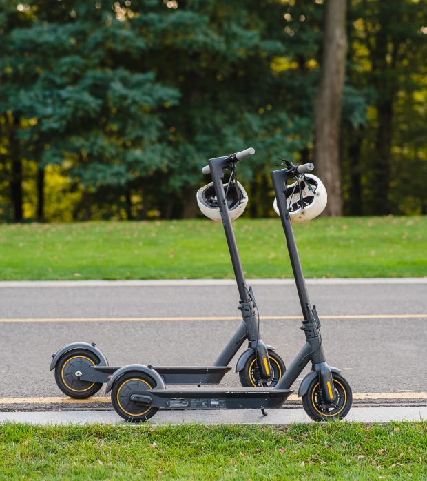 two electric kick scooters or e-scooter parked on the sidelines road in the park